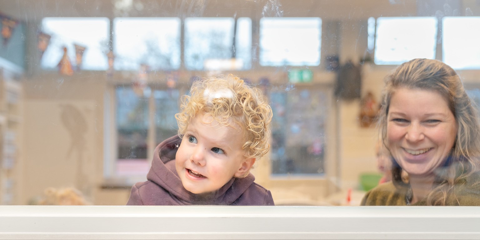 Kind kijkt nieuwsgierig door het raam op de kinderopvang
