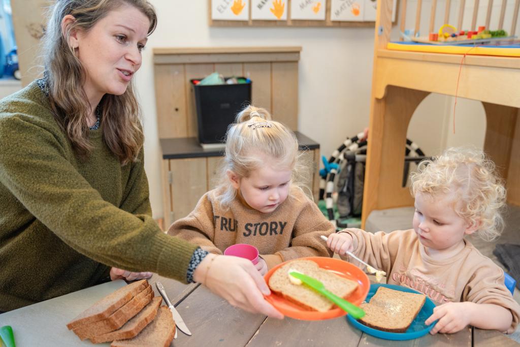 Pedagogisch medewerker eet samen met kinderen brood
