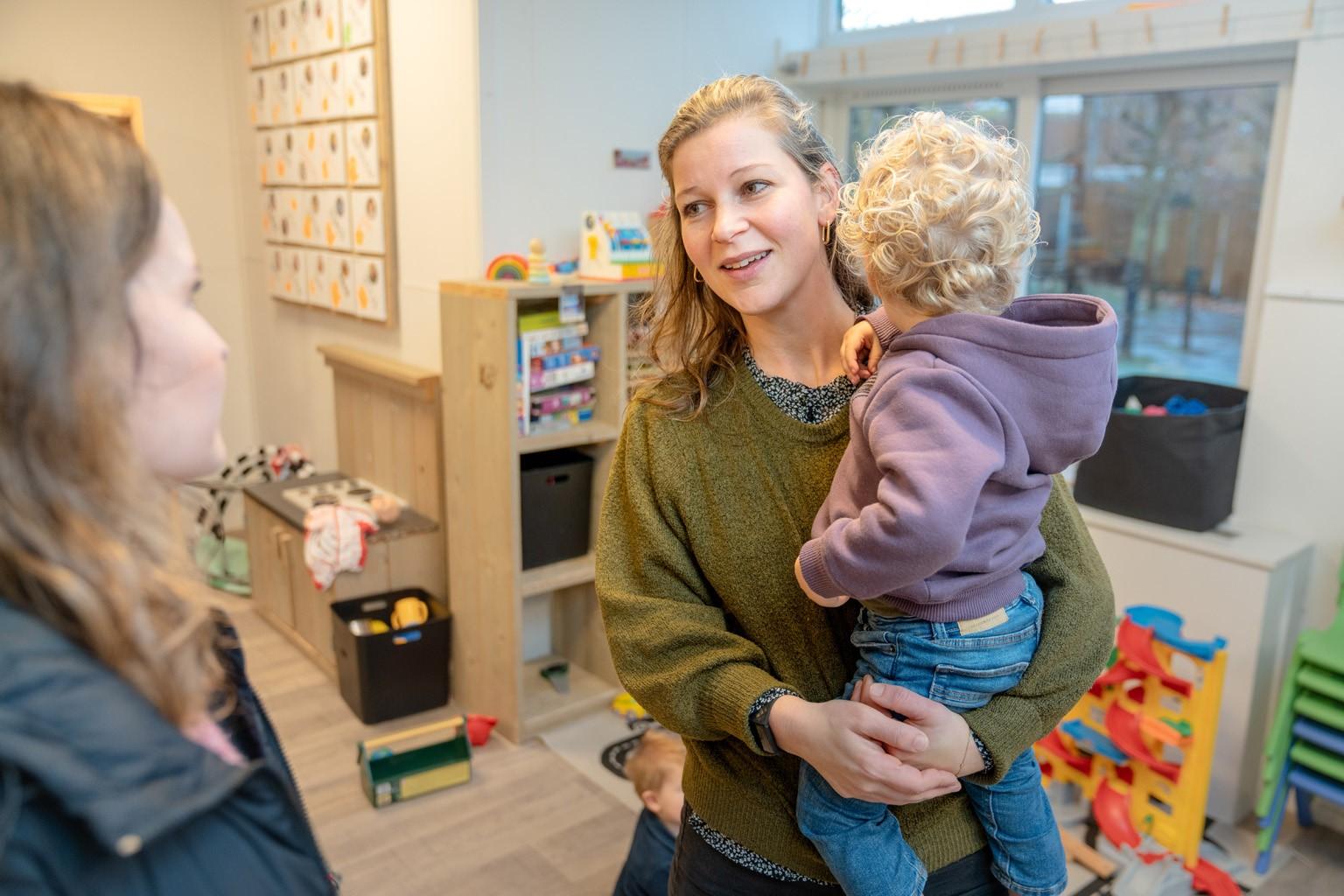 Pedagogisch medewerker heeft kind op de arm