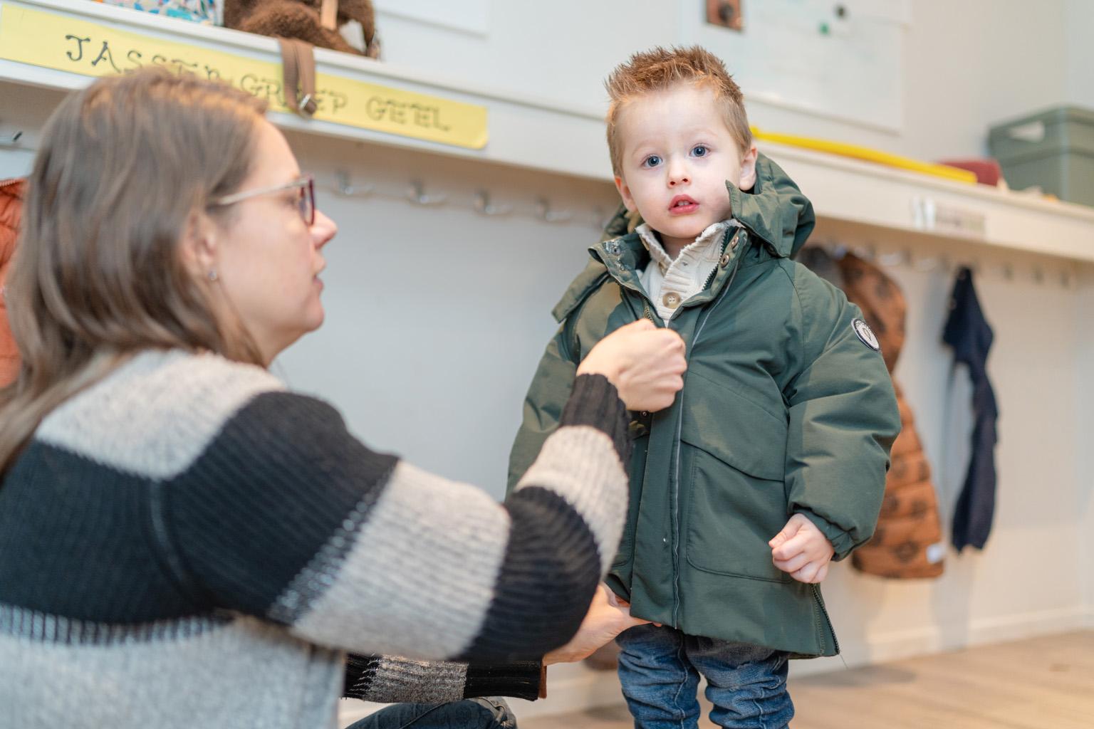 Pedagogisch medewerker trekt jas van kind dicht